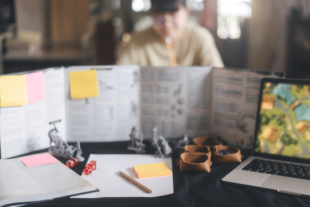 A Dungeon Master's screen in the foreground and teen girl playing in a D&D group therapy game in the background